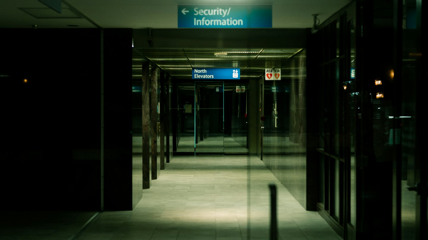 Empty office hallway with directional signs for elevators and security.